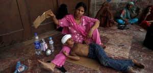 A woman uses a piece of cardboard to fan her son, while waiting for their turn for a medical checkup, outside Jinnah Postgraduate Medical Centre (JPMC) during intense hot weather in Karachi